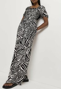 Czarny i biały kombinezon w zebrowy wzór, z kwadratowym dekoltem, bufiastymi rękawami i dopasowanym topem, z szerokimi, luźnymi spodniami.