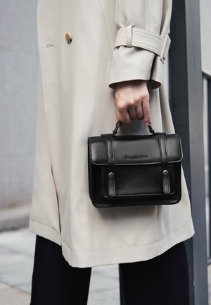 Zwarte leren handtas met een gestructureerde vorm, voorzien van een bovenhengsel, overslag klep en metalen accenten. Draagt een beige jas.