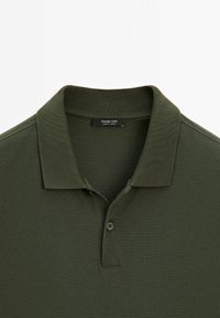 Polo shirt vert foncé en tissu texturé avec un col à côtes, doté d'une patte de boutonnage à trois boutons et d'une étiquette indiquant "Massimo Dutti."
