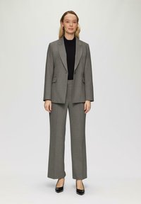 Grijze op maat gemaakte kostuum met een dubbelzijdige blazer met notch-revers en brede broekspijpen, gecombineerd met een zwarte top en zwarte hakken.