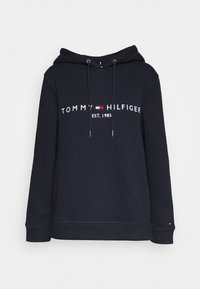 Hoodie bleu marine avec cordons, texte et logo blanc "Tommy Hilfiger EST. 1985" sur la poitrine, petit logo sur le poignet gauche.
