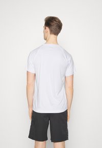 Camiseta deportiva para hombre en blanco, manga corta, tela suave, cuello redondo, combinada con pantalones cortos negros con un detalle lateral estampado.