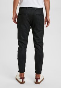 Černé pruhované kalhoty se slim fit střihem, s dvěma zadními kapsami. Ukázáno s ohrnutými lemy a v kombinaci s neformálními bílými a bordó teniskami.