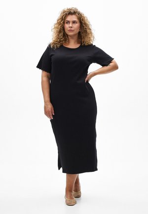 Robe midi noire côtelée avec des manches courtes et des fentes latérales, présentant un col rond et une texture douce. Portée avec des chaussures tissées de couleur claire.