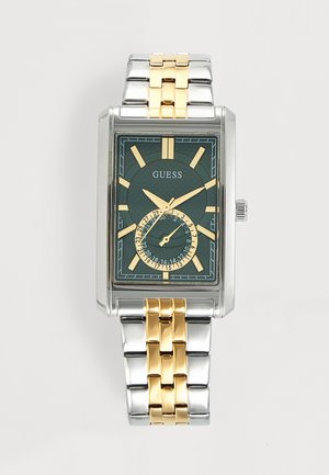 Montre-bracelet rectangulaire en métal argenté et doré Guess avec cadran vert foncé, index dorés et sous-cadran date à six heures.