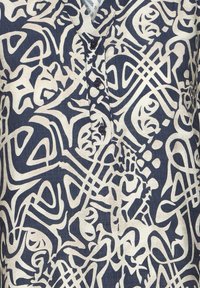 Marineblaue Stoffbluse mit abstrakten cremefarbenen Mustern. Sie verfügt über einen V-Ausschnitt und vier schwarze Knöpfe auf der Vorderseite.