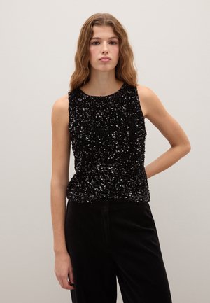 Schwarzes ärmelloses Oberteil, bedeckt mit Pailletten, mit rundem Ausschnitt. Kombiniert mit schwarzen Samthosen, die einen Texturkontrast betonen.