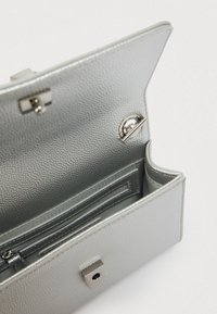 Srebrna torba od sintetičke kože, teksturirane vanjštine, otvorenog vrha koji otkriva organizirani unutarnji prostor s pretincima za kartice i džepom na patentni zatvarač.