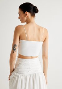 Top corto blanco de canalé con tirantes finos, que muestra una textura suave y un diseño ajustado, combinado con una falda blanca arrugada a juego.