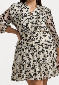 Blommig klänning med volang på halsringning och ärmar, tillverkad av lättviktsmaterial, i creme med svarta lövmönster och justerbart snöre i midjan.