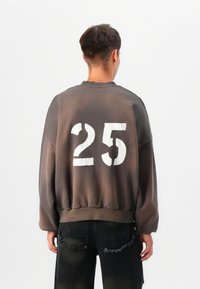 Sweatshirt cinzento oversized com o número "25" em destaque e desbotado, exibido na parte de trás. O design apresenta um colarinho e punhos canelados.