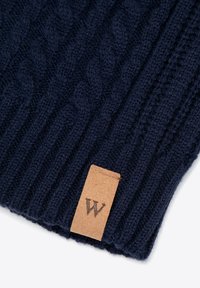 Berretto lavorato a maglia blu navy con motivo a trecce strutturato, bordi a costine e una toppa in pelle tan con logo "W" in rilievo.