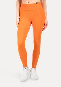 Fel oranje leggings van rekbaar materiaal met een gladde textuur, voorzien van een hoge tailleband en minimalistische branding op de heup.