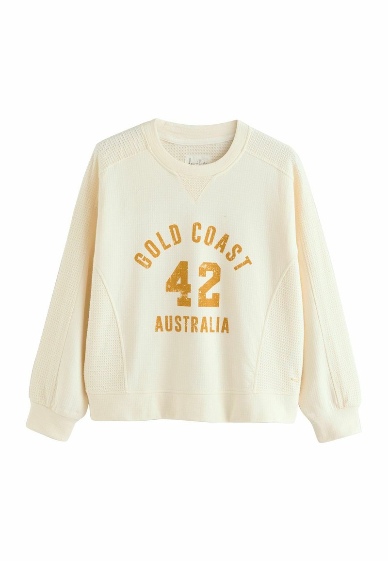 Krämfärgad sweatshirt med texturerad tyg, raglanärmar och tryckt text: "GOLD COAST 42 AUSTRALIA" i guld.