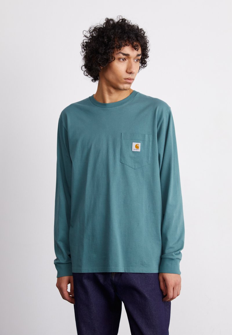 Camisa de manga larga en color turquesa con un bolsillo; fabricada en algodón; cuenta con un parche de logo cuadrado en el pecho; diseño ajustado con mangas con puños.