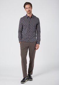 Camisa de manga larga en azul con un patrón geométrico de rectángulos en marrón, beige y azul marino; combinada con pantalones marrones texturizados y zapatillas oscuras.