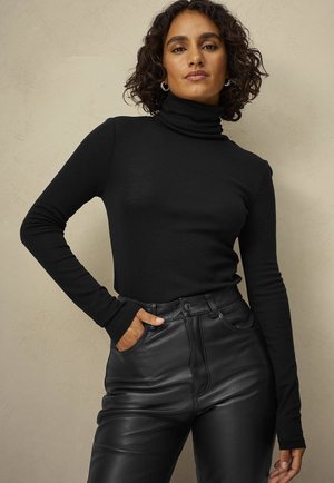 Sort turtleneck sweater med lange ærmer, lavet af et blødt stof; parret med højtaljede sorte faux læderbukser med synlige syninger.