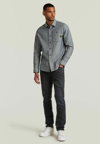 Chemise grise à boutons avec une poche poitrine, associée à un jean noir délavé et des baskets blanches. Design décontracté, ajusté et en tissu texturé.