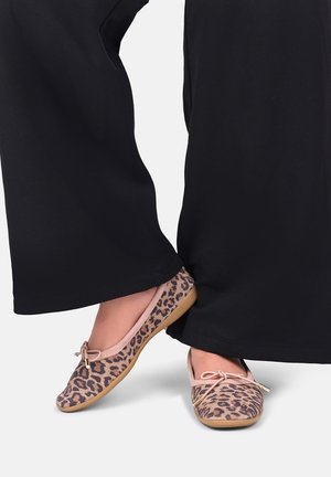 Voeten met ballet flats in luipaardprint met roze rand en strikjes, gecombineerd met zwarte broek met wijde pijpen.