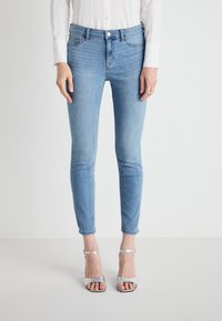 Világoskék, skinny fazonú farmernadrág, elülső zsebekkel, gombos záródással és sima textúrával, ezüst színű pántos szandálokkal párosítva.