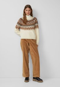 Crème trui met een geometrisch bruin patroon op de schouders, gecombineerd met tan corduroy broek en zwarte plateauboten.