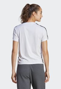 Witte sportieve t-shirt met zwarte schouderstrepen, korte mouwen en een gladde textuur. Gecombineerd met grijze joggingbroeken in een comfortabele pasvorm.