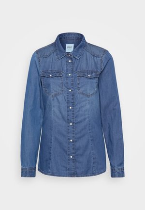 Džínová košeľa v stredne modrej farbe, s dlhými rukávmi, zapínaním na gombíky vpredu, dvoma náprsními vreckami a kontrastným prešívaním na pleciach.