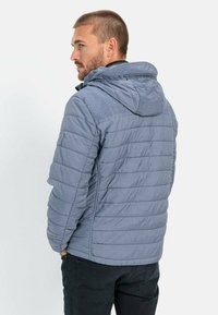 Grå, quilted jakke med hætte, fremstillet i et tekstureret, letvægts stof. Inkluderer sidelommer og elastiske manchetter. Bagview.