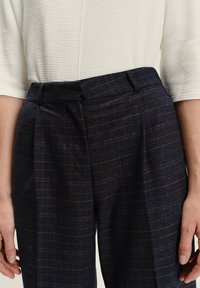 Dunkelnavy, gemusterte Hose mit hohem Bund, strukturiertem Stoff, Falten an der Vorderseite und einem sauberen Taillenbandabschluss.