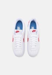 Hvide sportssko med røde detaljer og Nike-logo, der har en glat tekstur, snørebåndsdesign og en blå inderforing.