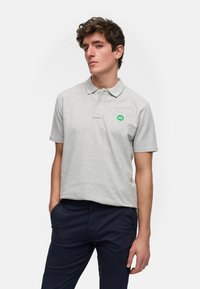 Lys grå polo skjorte laget av bomull, med krage og en strukturert overflate. Den har en liten grønn logo på venstre brystområde.
