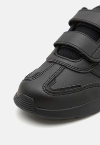 Basket noire avec un dessus en cuir lisse, des panneaux en maille, deux sangles Velcro et une semelle en caoutchouc texturée avec des rainures diagonales.