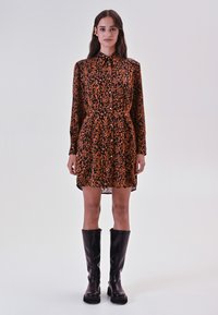 Robe imprimée léopard en orange et noir avec un devant à boutons, des manches longues et une taille cintrée ; associée à des bottes noires montantes.