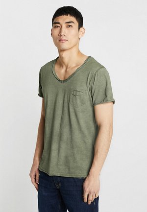Olivgrünes Baumwoll-T-Shirt mit V-Ausschnitt und umgeschlagenen Ärmeln, das über eine kleine Brusttasche und einen lockeren Schnitt verfügt. Der Stoff hat eine leicht strukturierte Oberfläche.