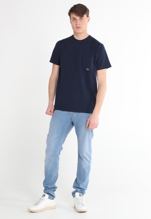 T-shirt in cotone blu navy con scollatura a girocollo, maniche corte e taschino sul lato sinistro del petto con una toppa a forma di triangolo.