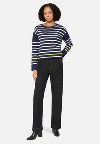 Marineblauw en wit gestreepte gebreide trui met groene accenten; gecombineerd met high-waisted donkere spijkerbroek met goudkleurige knoopdetails.