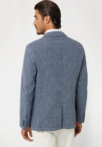 Mėlynas lininis bleizeris su tekstūruotu paviršiumi, su išpjautomis apykaklėmis ir trimis sagutėmis kiekviename rankogalyje. Yra vienas nugaros ventiliacijos atidarymas ir pritaikytas siluetas.