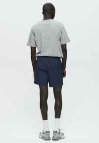 T-shirt grigio a maniche corte abbinato a pantaloni corti blu navy, mostrato dal retro. Il modello indossa sneakers grigie e calzini bianchi, con uno sfondo pulito.