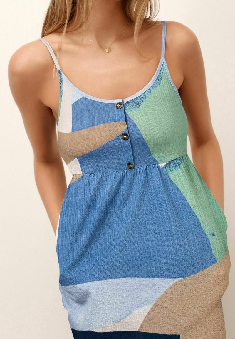 Femme portant une robe sans manches boutonnée avec des blocs de couleurs abstraits bleu, vert, beige et blanc et des bretelles fines.