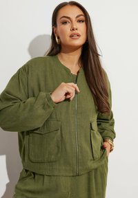 Giacca bomber verde oliva con zip frontale, scollatura rotonda e due tasche anteriori. Realizzata in tessuto leggero e dalla texture interessante.