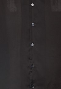 Zwarte shirt van gladde stof met een knoopsluiting met zes gelijkmatig verdeelde knopen aan de voorkant. Geen patronen of versieringen.