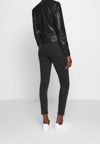 Zwarte leren jas met een aansluitend ontwerp, gecombineerd met donker strakke jeans en witte sneakers. Voorzien van beschadigde zoom en subtiele stiksel details.