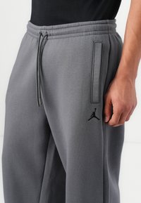 Gray sweatpants made of soft fabric, featuring an elastic waistband, drawstring, side pockets, and a black Jumpman logo on the left thigh.