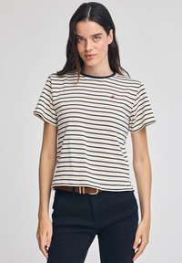 Randig t-shirt i beige med marinblå ränder, rund halsringning, korta ärmar och liten röd logotyp på vänster bröst. Mjukt bomullsmaterial.