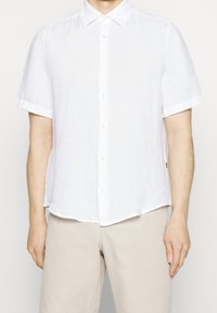 Camicia bianca a maniche corte in lino con chiusura a bottoni, con polsini ripiegati e una vestibilità rilassata. Texture morbida, design casual e leggero.