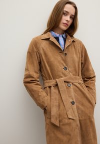 Trench coat in suede marrone con vita cinchata, chiusura a bottoni e tasche laterali. Presenta un colletto classico e una texture liscia.