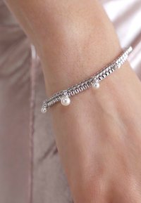 Bracelet en argent avec un design de chaîne délicate et deux petites perles attachées. Le bracelet est porté sur un poignet nu.