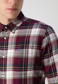 Karierte Button-up-Hemden in Burgunderrot, Grau und Marineblau. Verfügt über eine Brusttasche und ein markiertes Etikett sowie einen weichen, strukturierten Stoff.