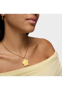 Collana d'oro con un pendente a forma di fiore su una delicata catena. Il pendente presenta una texture liscia e piatta e una finitura metallica brillante.