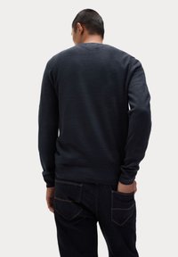 Dunkelblauer Pullover mit glatter Textur, langen Ärmeln, gerippten Bündchen und Saum. Über dunklen Jeans getragen, zeigt ein minimalistisches Design.